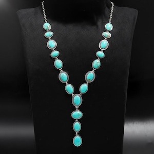 May include: A silver necklace featuring oval turquoise stones. The pendant has a Y-shape design, with the stones set in silver metal. The necklace is displayed on a black mannequin.