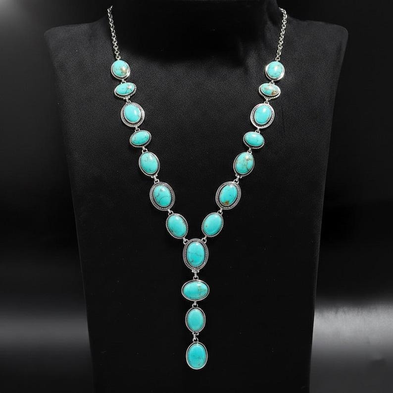 May include: A silver necklace featuring oval turquoise stones. The pendant has a Y-shape design, with the stones set in silver metal. The necklace is displayed on a black mannequin.