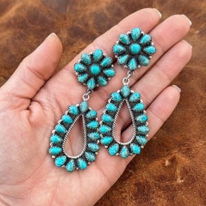 May include: A pair of dangle earrings featuring a circular cluster of small, oval-shaped turquoise stones at the top, connected to a larger, pear-shaped open frame also lined with turquoise stones, all set in a silver-toned metal setting.