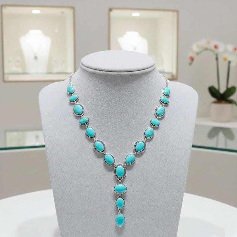 May include: A silver necklace featuring oval turquoise stones. The stones are set in a silver frame and arranged in a cascading design. The necklace is displayed on a white bust, highlighting its elegant design.