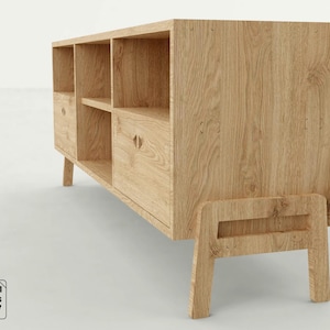 Puede incluir: Un mueble de madera de color claro con múltiples estantes abiertos y dos cajones. El mueble tiene forma rectangular con un diseño moderno de mediados de siglo. El mueble está hecho de madera de color claro y tiene un acabado natural. El mueble está soportado por cuatro patas.