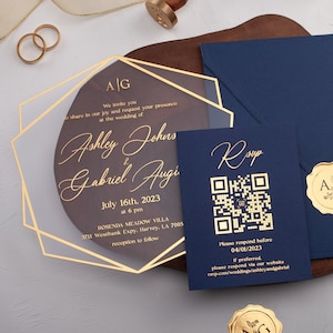May include: A gold and blue wedding invitation suite with a clear acrylic invitation featuring the couple's names and wedding date. The RSVP card has a QR code and the text "RSVP" in gold script.