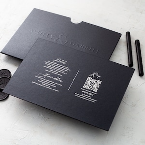 May include: A black wedding invitation suite featuring embossed names "Ashley & Gabriel". Includes invitation, envelope, wax seals, and black sticks. The invitation has details and a QR code. The date is 04/01/2023.