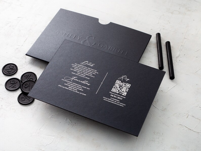 May include: A black wedding invitation suite featuring embossed names "Ashley & Gabriel". Includes invitation, envelope, wax seals, and black sticks. The invitation has details and a QR code. The date is 04/01/2023.