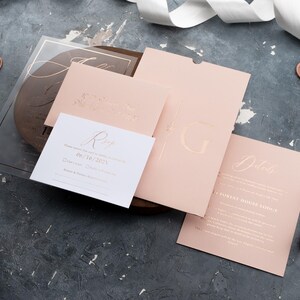 Blush pink wedding stationery flat lay with a clear acrylic invitation, sleeve envelope and optional printed RSVP and details cards.