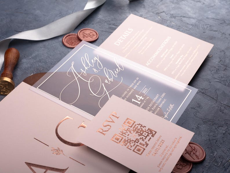 Angled view of a clear acrylic wedding invitation, blush pink sleeve envelope and optional rose gold foil QR RSVP and details cards.