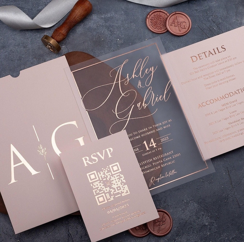 Clear acrylic wedding invitation with rose gold foil, blush pink sleeve envelope, optional QR RSVP card and details card arranged on a dark background.