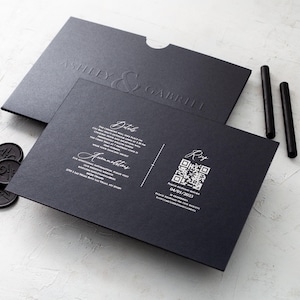 A black wedding invitation with copper script and a black envelope with embossed names, along with a black RSVP card featuring a QR code, are arranged on a white textured surface.