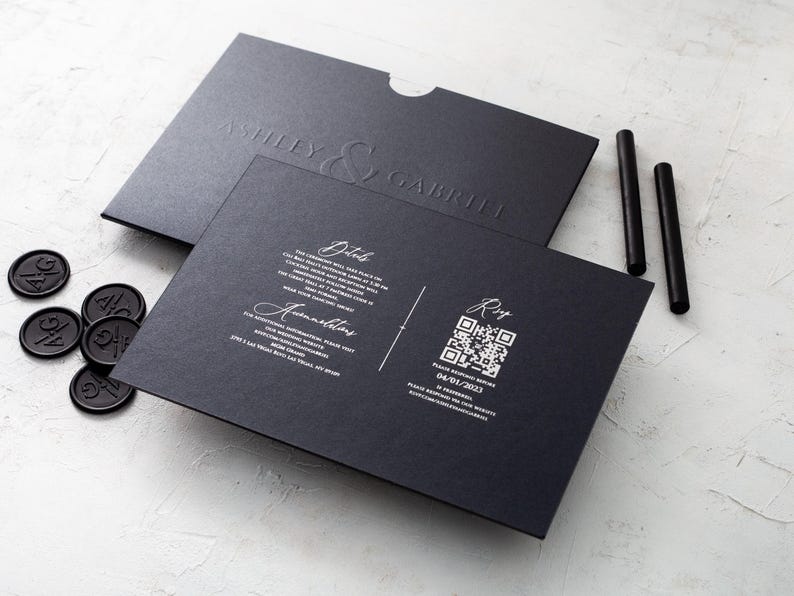 A black wedding invitation with copper script and a black envelope with embossed names, along with a black RSVP card featuring a QR code, are arranged on a white textured surface.