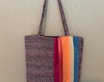 May include: A black and white tweed tote bag with a rainbow stripe of fabric on the side. The stripe is made of velvet, orange, and blue fabric.