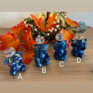 May include: Four blue dragon figurines with clear glass globes on their heads. Each globe contains a small, colorful, plastic fish. The figurines are sitting on a wooden surface.
