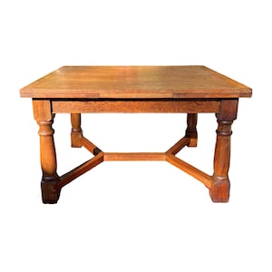 May include: A square, wooden coffee table with a warm, medium-brown finish. The table features a solid top and four turned legs connected by an X-shaped stretcher. The table measures approximately 30 inches in length and width.