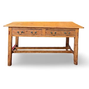 May include: A light brown wooden table with two drawers and brass handles. The table has a rectangular top and four sturdy legs. The wood grain is visible, giving it a rustic appearance. The table is likely a piece of furniture for a living room or dining room.