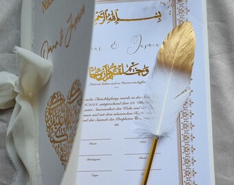 May include: A white Nikkah certificate with gold calligraphy and a gold and white feather pen. The certificate is decorated with a gold heart design and the text "Nikkah Zertifikat" is written in gold lettering. The text "Und wir haben auch in Enaren erachaffen." is written in gold lettering.