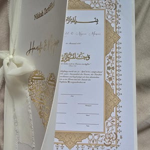May include: A white Nikkah certificate with gold calligraphy and decorative borders. The certificate includes the names "Hanifi & Najwa" and the date "20. Shawwal 1446". The text "بسم الله الرحمن الرحيم" is written in Arabic script.