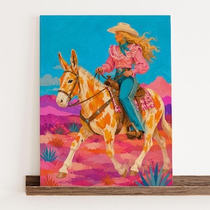 May include: A vibrant painting on canvas depicting a person with long blonde hair wearing a white cowboy hat, a pink ruffled shirt, and blue jeans riding a spotted brown and white mule. The background features a desert landscape with pink mountains.