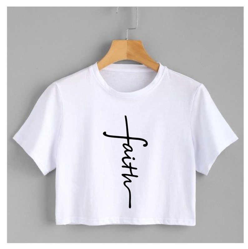 May include: White cropped t-shirt with a black graphic of a cross with the word "faith" written vertically.