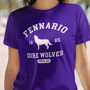 May include: Purple t-shirt with a white graphic of a wolf howling at the moon. The graphic also includes the text "Fennario 19 65 Dire Wolves PHYS. ED."