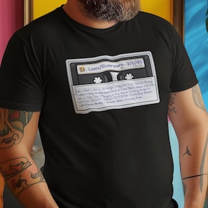 May include: A black t-shirt with a graphic of a cassette tape. The tape is labeled "St. Louis/Riverport - 7/5/95" and has handwritten track listings.