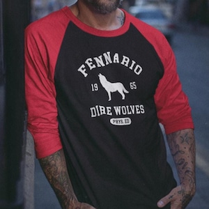 May include: Black and red raglan-style long-sleeve shirt. The shirt features the text "Fennario 1965 Dire Wolves Phys. Ed." with a howling wolf graphic. The sleeves are red, and the body is black.