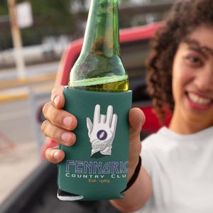 May include: A teal drinks koozie featuring a white golf glove design and the text "Fennaris Country Club Est. 1965". The koozie holds a green glass bottle.