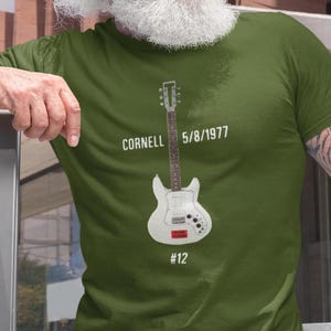 May include: A green t-shirt with a white electric guitar, the text "Cornell 5/8/1977 #12" and a red sticker on the guitar.