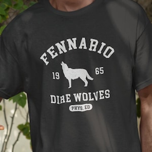 May include: A dark gray t-shirt with a white wolf howling at the moon. The text "Fennario 19 65 Dire Wolves Phys. Ed" is printed on the shirt.