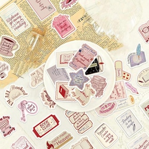 Könnte beinhalten: Eine Sammlung von buchbezogenen Aufklebern mit verschiedenen Illustrationen und Texten, darunter Phrasen wie please go away I am reading, book marks and daydreams und ask me about my books, präsentiert auf einem weißen Teller.
