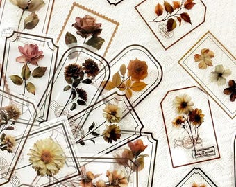 May include: A collection of transparent rectangular stickers featuring pressed dried flowers and vintage postal stamp designs. Each sticker displays various botanical specimens in shades of brown, orange, and cream, framed by thin brown borders.