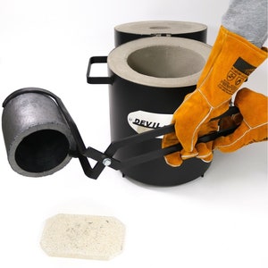 Puede incluir: Un crisol de metal negro con un asa, una pinza de metal negro y un ladrillo de cer&aacute;mica blanco. El crisol est&aacute; etiquetado con "DEVIL".