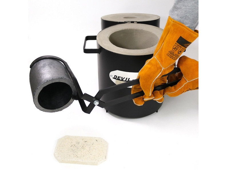 Puede incluir: Un crisol de metal negro con un asa, una pinza de metal negro y un ladrillo de cer&aacute;mica blanco. El crisol est&aacute; etiquetado con "DEVIL".