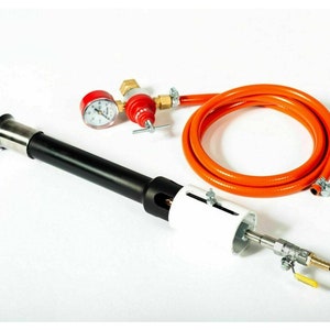 Puede incluir: Una antorcha negra y plateada con una válvula blanca y plateada, un manómetro rojo y una manguera naranja. La antorcha se utiliza para calentar y soldar.