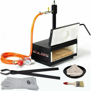 May include: A black metal forge with an orange hose and a pressure gauge. The forge has a white refractory lining and a small opening for inserting metal. The forge is labelled "Devil Forge". The image also shows a pair of tongs, a pair of leather gloves, a small plate of refractory mortar, and a paintbrush.