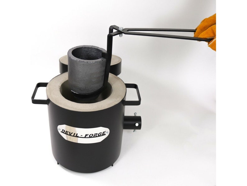 Puede incluir: Un horno de crisol de metal negro con un crisol extra&iacute;ble y un asa. El horno tiene una etiqueta que dice "DEVIL-FORGE".