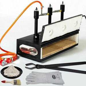 May include: A black metal gas forge with a white refractory lining and a red and orange gas hose. The forge is labelled "Devil-Forge". The image also shows a pair of black tongs, a pair of grey leather gloves, a small bowl of grey refractory mortar, and a paintbrush.