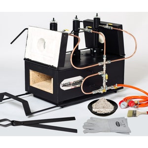 May include: A black metal forge with a white refractory brick lining. It has two gas burners and a copper piping system. The forge is on a metal stand with wheels. The image also shows a pair of tongs, a bag of refractory mortar, a pair of welding gloves, a paintbrush, and a pressure gauge.