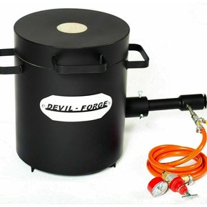 Puede incluir: Horno de metal negro con tapa redonda y un asa a cada lado. El horno tiene una etiqueta blanca que dice "DEVIL-FORGE". Un tubo de metal negro se conecta al horno y una manguera roja y naranja se conecta al tubo. La manguera tiene un man&oacute;metro y un regulador.