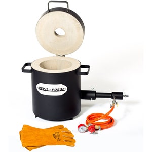 Puede incluir: Un horno de metal negro con una tapa de cerámica blanca, una manguera negra y naranja y dos manómetros. El horno tiene el texto "DEVIL-FORGE" en el lateral. El horno se acompaña de un par de guantes de soldadura de cuero marrón.