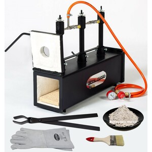 May include: Black metal gas forge with a white refractory brick lining, a red pressure gauge, and a black handle. The forge is on a white surface. The image also shows a pair of black tongs, a pair of grey leather welding gloves, a small plate of grey refractory mortar, and a red and white paint brush.
