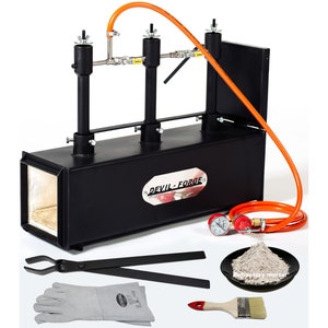 May include: A black metal forge with two burners and a red and white label that says "DEVIL-FORGE". The forge is accompanied by a pair of tongs, a pair of welding gloves, a small plate of refractory mortar, and a paintbrush.