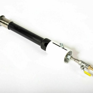 Puede incluir: Un quemador de gas negro y plateado con una válvula blanca y una manija amarilla. El quemador tiene un cuerpo largo y cilíndrico y una base redonda y blanca.