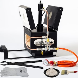 Puede incluir: Un horno de gas de metal negro con un sistema de tuberías de cobre y una tapa extraíble. El horno está sobre un soporte e incluye un par de tenazas, un par de guantes, un manómetro, una manguera, una bolsa de mortero refractario y una brocha.