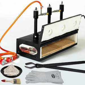 Puede incluir: Un horno de gas de metal negro con un revestimiento refractario blanco y una manguera de gas roja y naranja. El horno está etiquetado como "Devil-Forge". La imagen también muestra un par de tenazas negras, un par de guantes de cuero grises, un pequeño cuenco de mortero refractario gris y un pincel.