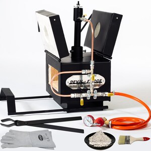 May include: A black metal gas forge with a copper pipe system and a black lid. The forge is on a black metal stand. The forge comes with a pair of tongs, a pair of gloves, a pressure gauge, a hose, a bag of refractory mortar, and a paint brush.