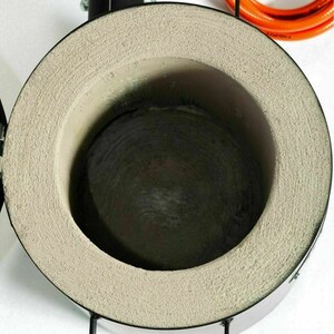 Puede incluir: Primer plano del interior de un peque&ntilde;o horno redondo de metal con un revestimiento gris texturizado. El horno se utiliza para fundir metal.