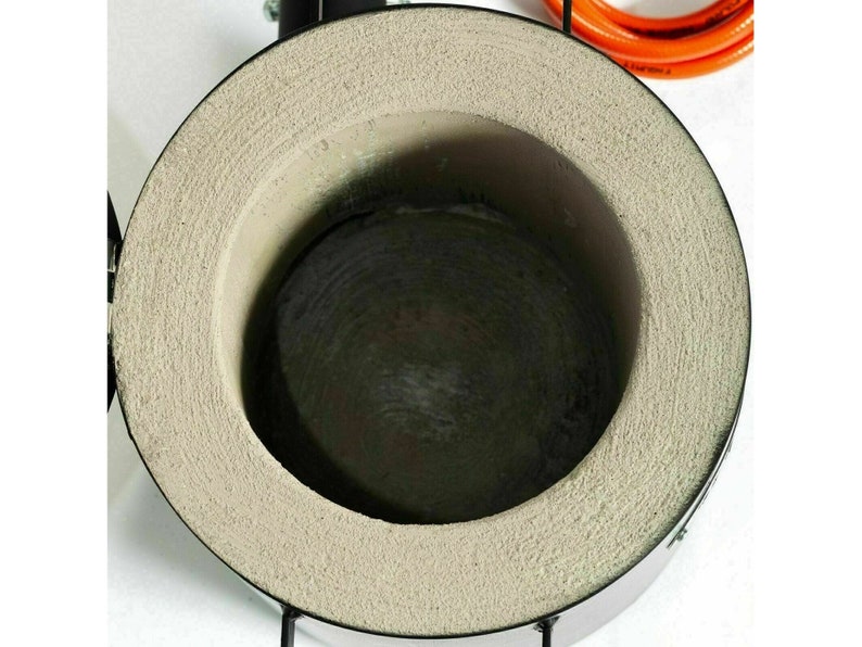 Puede incluir: Primer plano del interior de un peque&ntilde;o horno redondo de metal con un revestimiento gris texturizado. El horno se utiliza para fundir metal.