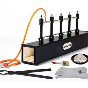 May include: A black metal forge with four burners and a  "DEVIL-FORGE" label. The forge is accompanied by a pair of tongs, a brush, a pair of leather gloves, and a small plate of refractory mortar.