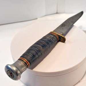May include: A vintage hunting knife with a brown leather handle and a silver metal pommel. The blade is made of steel and has a slight curve.