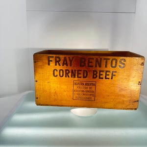 May include: A wooden box with the words "Fray Bentos Corned Beef" printed on the front. The box is labelled "Industria Argentina Ministerio de Agricultura y Ganaderia Establecimiento N°15 Inspeccionado".
