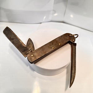 May include: A rusty multi-tool with a blade, a hook, and a small blade. The tool is open and the hook is extended.